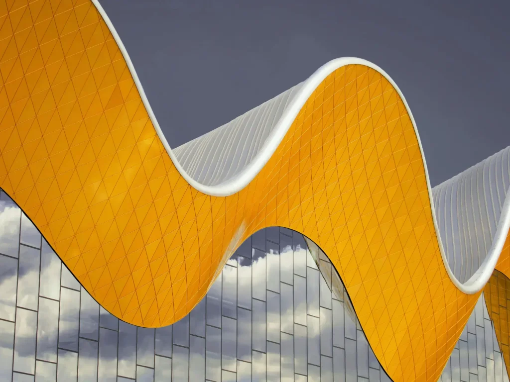Curved yellow architectural feature with a wavy design against a cloudy sky. The Narrative Group.