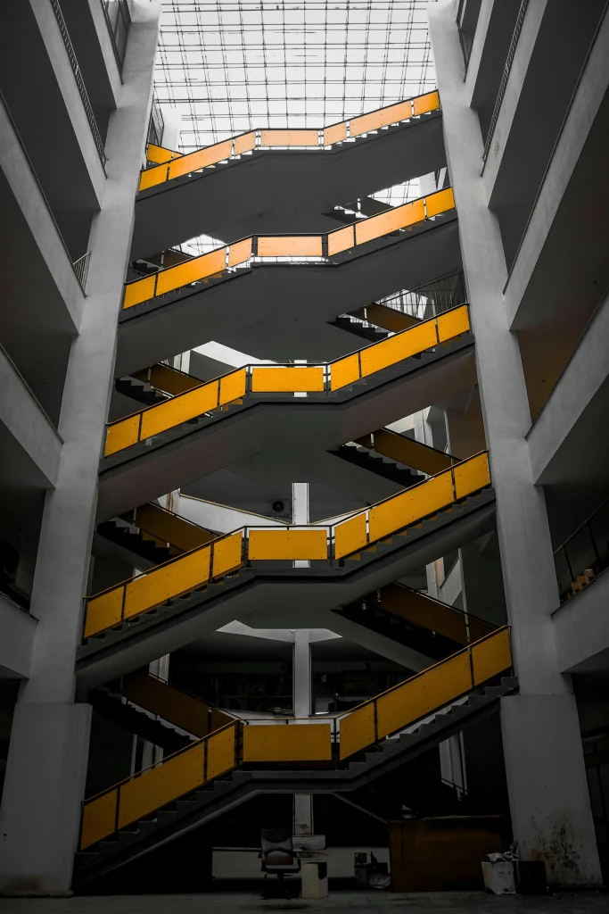 Interior view of a multi-level staircase featuring yellow handrails and a modern architectural design. The Narrative Group.