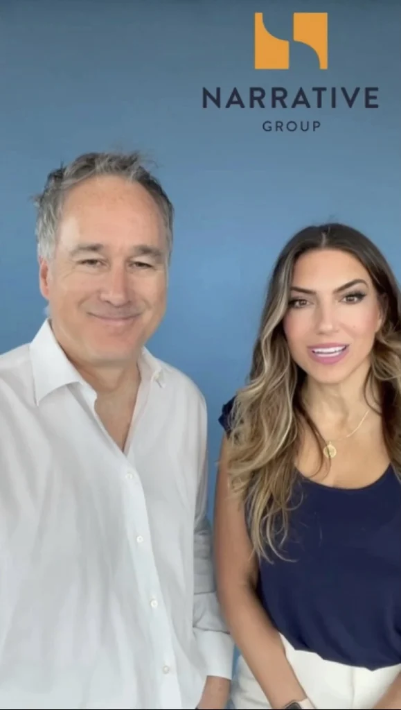 Two individuals standing together in front of a blue background with the Narrative Group logo above them. The Narrative Group.