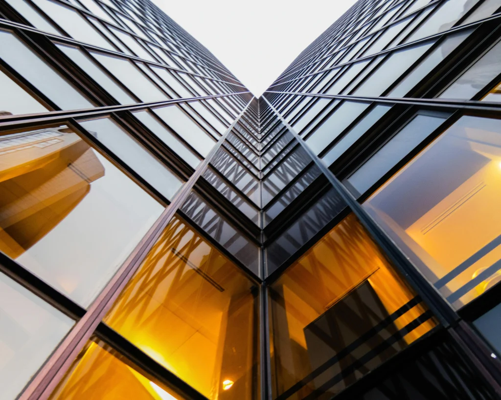 View of a modern glass building from the ground, showcasing reflective windows and structural lines. The Narrative Group.