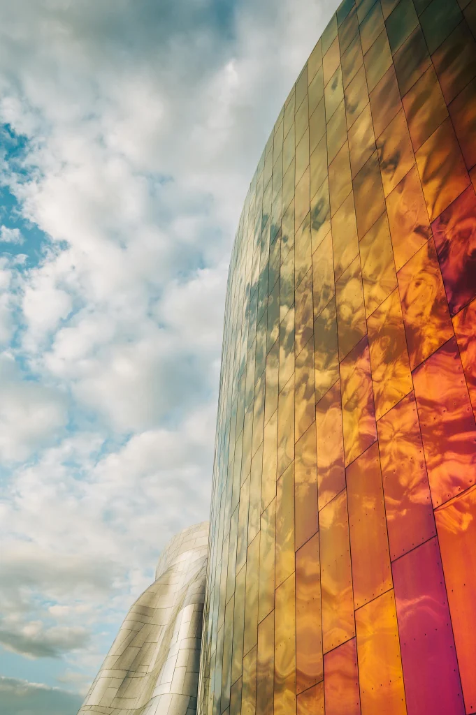 Curved building with a reflective orange and gold facade under a cloudy sky. The Narrative Group.