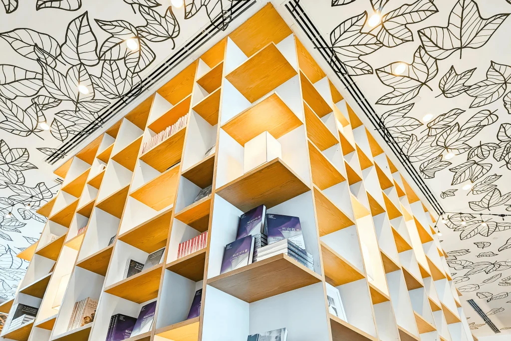 Contemporary bookshelf design with a leaf-patterned ceiling in a well-lit space. The Narrative Group.