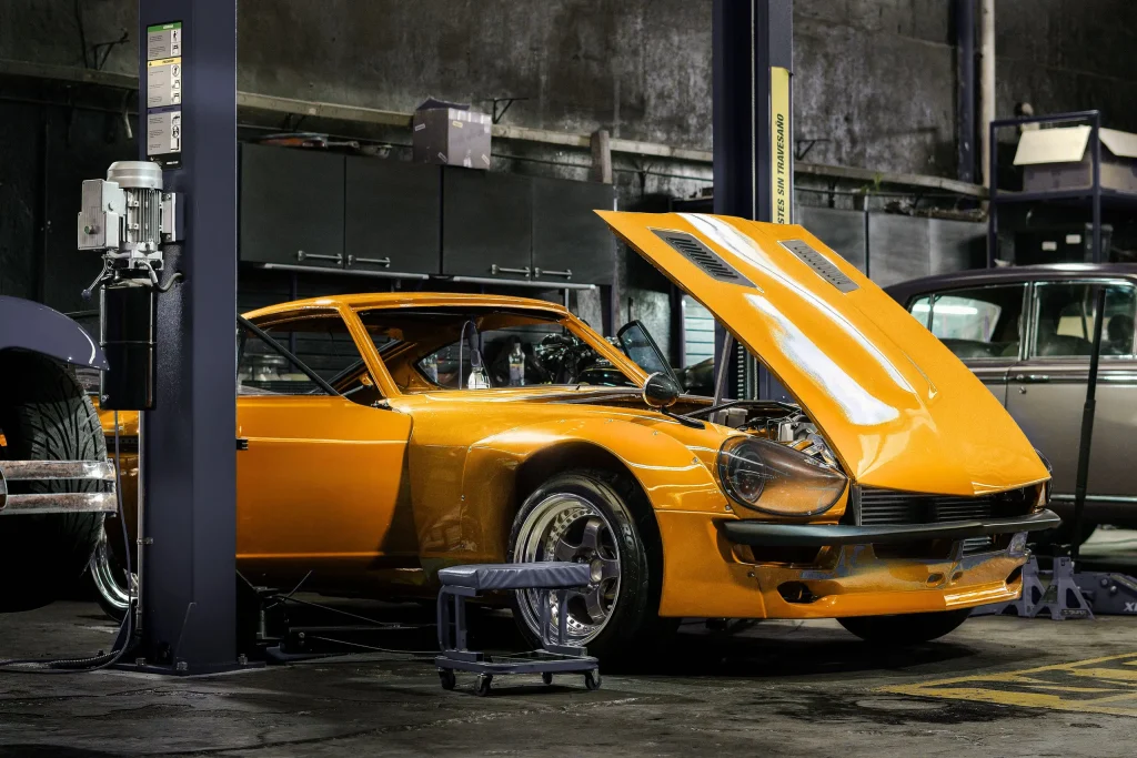 Orange car lifted in an industrial service bay with equipment and diagnostic screens, supporting it modernization and technology adoption.
