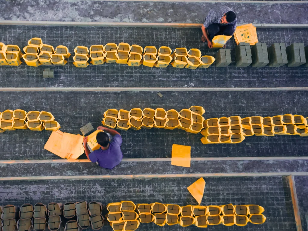 Overhead view of warehouse workers stacking yellow and gray packages in organized rows, supporting it cost reduction goals.